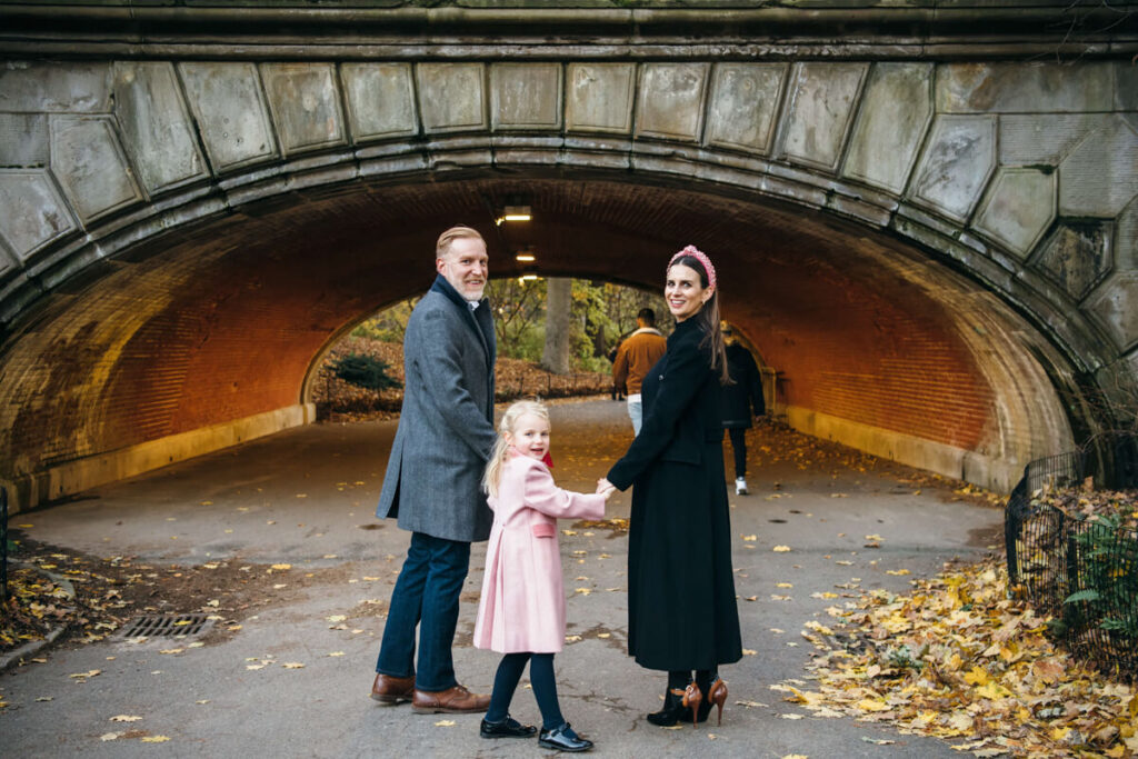 Husband and wife and their daughter hold hands in their winter coats as they look back and smile at the camera behind them. Photographed in Central Park.

Manhattan Family Portraits. Central Park Family Photography. NYC Family Photographer.