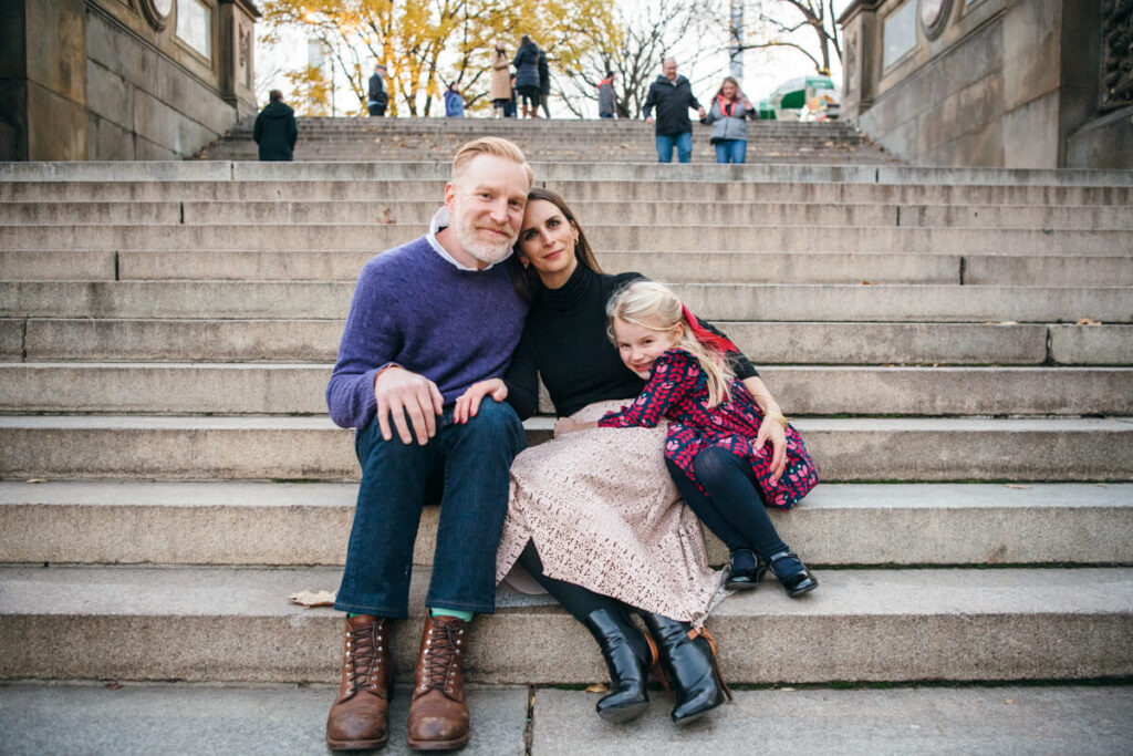 Husband, wife, and their daughter sit on steps in Central Park. The daughter hugs her mother. They are smiling at the camera. Photographed in Central Park.

Manhattan Family Portraits. Central Park Family Photography. NYC Family Photographer.