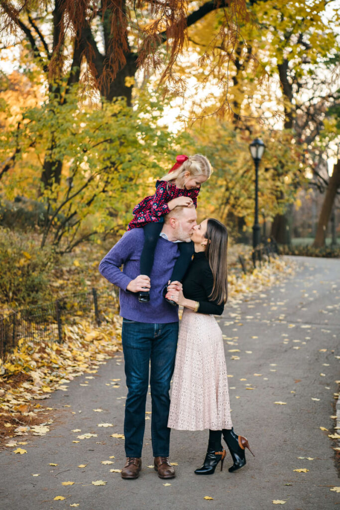 Man has his daughter on his shoulders as he kisses his wife. Photographed in Central Park.

Manhattan Family Portraits. Central Park Family Photography. NYC Family Photographer.