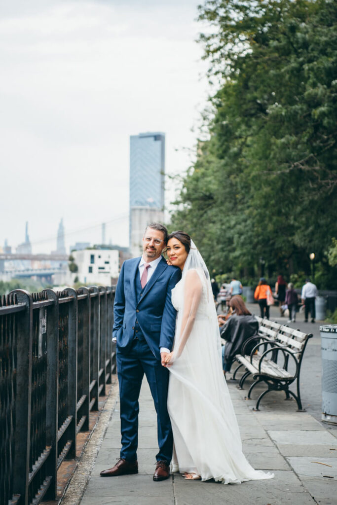 Bride and groom stand beside each other on the Brooklyn Heights Promenade. They are holding hands and her head is resting on his shoulder as they both smile at the camera.

NYC Wedding Portraits. Brooklyn Wedding Photographer. Luxury Local Wedding Photography.