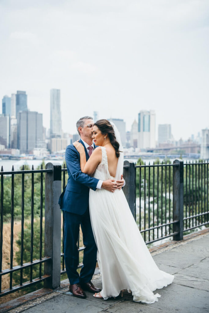 Bride and groom stand in each other's arms in the Brooklyn Heights Promenade as he kisses her on the head.

NYC Wedding Portraits. Brooklyn Wedding Photographer. Luxury Local Wedding Photography.