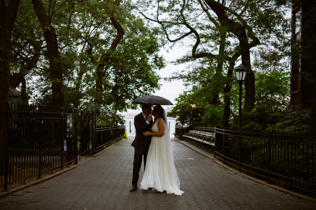 Bride and groom stand under a black umbrella at an entrance to the Brooklyn Heights Promenade and kiss.

NYC Wedding Portraits. Brooklyn Wedding Photographer. Luxury Local Wedding Photography.