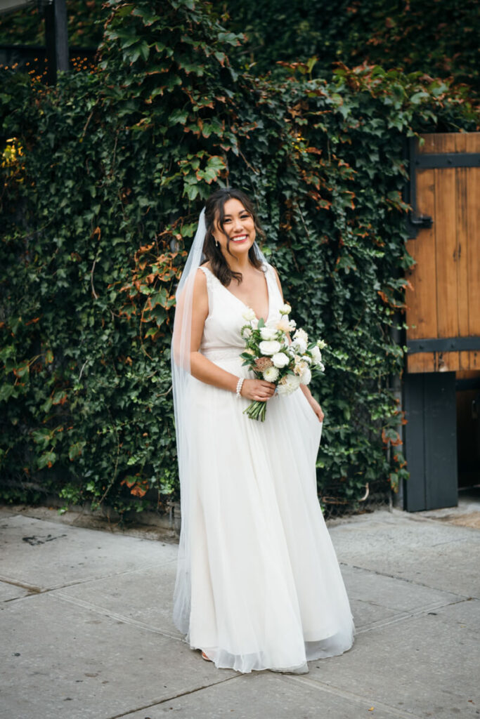 Bride stands in front of an ivy-covered wall in her wedding dress, veil, and holding a bouquet of flowers. She smiles at the camera.

NYC Wedding Portraits. Brooklyn Wedding Photographer. Luxury Local Wedding Photography.