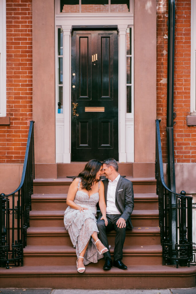 A man and woman sit on a stoop in New York City. She has a hand on his leg and they are smiling and touching foreheads.

NYC Engagement Portraits. Manhattan Engagement Photographer. 