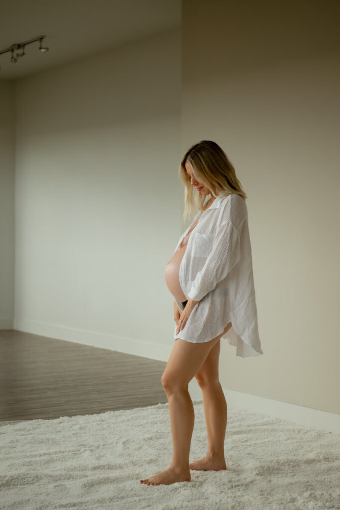 Pregnant woman is standing on a fluffy rug, wearing only a white button down, looking down at her baby bump and smiling.

Austin Maternity Photography. Austin Maternity Photographer. Austin Maternity Portraits. 