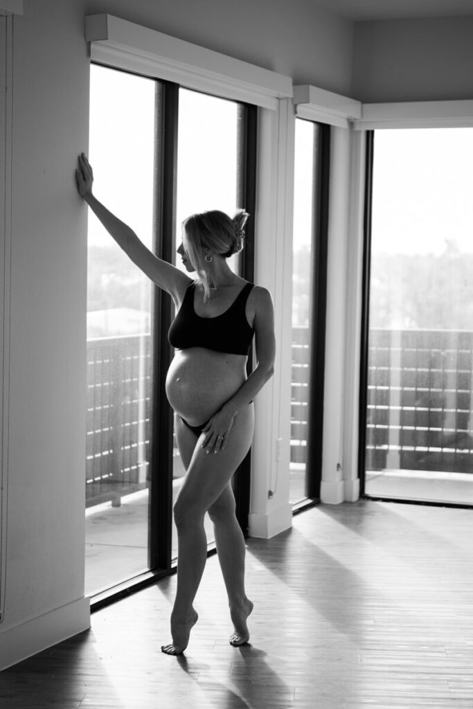 Pregnant woman stands next to a window on her tiptoes with her hand reaching above her on the wall, wearing black underwear and black bra.

Austin Maternity Photography. Austin Maternity Photographer. Austin Maternity Portraits. 