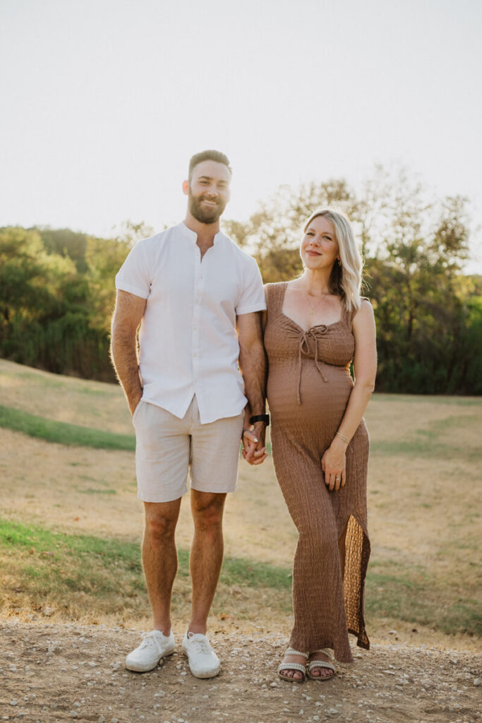 Husband and pregnant wife stand next to each other in a field, holding hands and smiling at the camera. Maternity session photographed at Zilker Park in Austin.

Zilker Maternity Portraits. Austin Photography. Zilker Maternity Photographer.