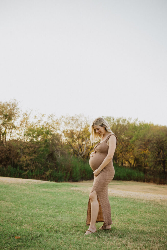Pregnant woman lookd down and smiles as she holds her baby bump and walks across a field. Maternity session photographed at Zilker Park in Austin.

Zilker Maternity Portraits. Austin Photography. Zilker Maternity Photographer.