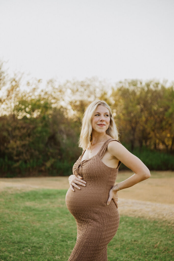 Pregnant woman has one hand on hip and the other hand on her belly. She is smiling off to the side. Maternity session photographed at Zilker Park in Austin.

Zilker Maternity Portraits. Austin Photography. Zilker Maternity Photographer.