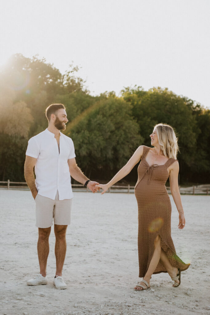 Husband and pregnant wife stand smiling and holding each other's hand, wife walking toward her husband. Maternity session photographed at Zilker Park in Austin.

Zilker Maternity Portraits. Austin Photography. Zilker Maternity Photographer.
