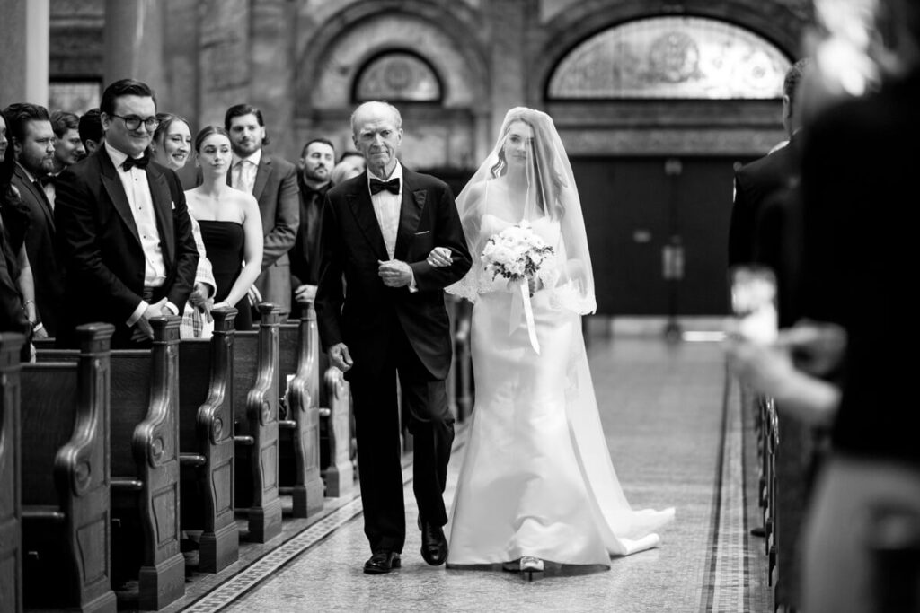 Bride and her father walk down the aisle of the Church of St. Ignatius Loyola while guests look on and smile. Black and white photograph.

Luxury NYC Wedding Photography. Manhattan Luxury Wedding Photographer. NYC Luxury Wedding. University Club Wedding Photographer.