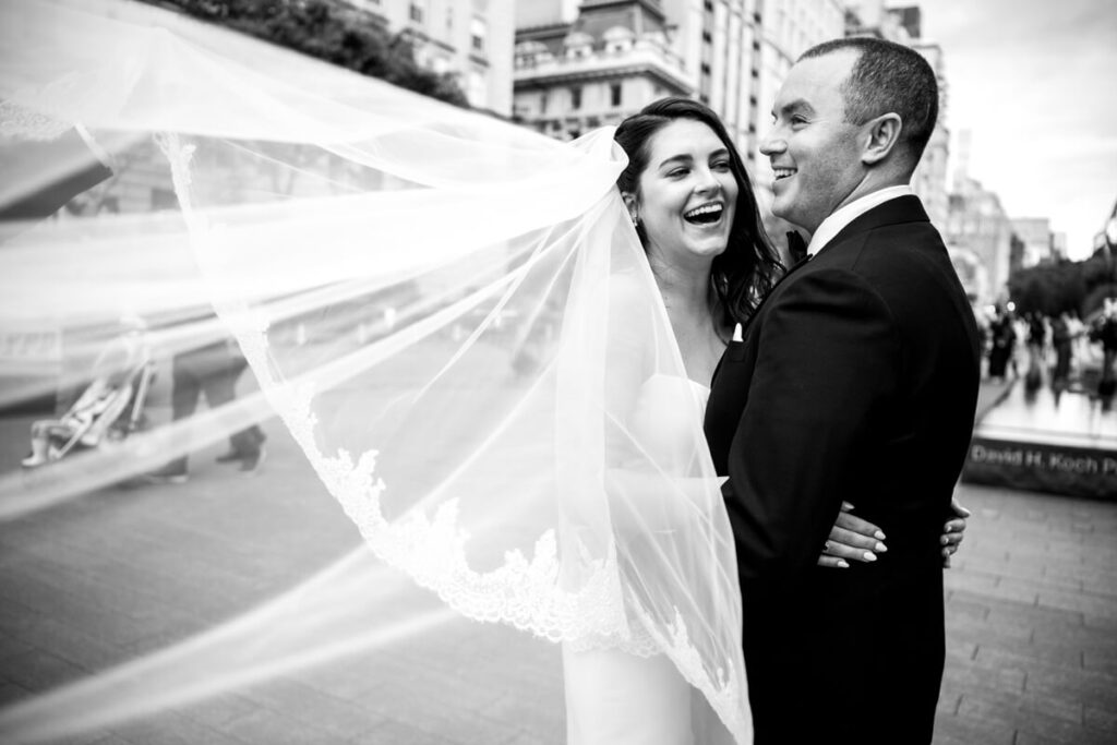 Bride and groom look at each other and smile outside the Metropolitan Museum of Art on 5th Avenue in Manhattan. The bride's veil is swooping toward the camera in the wind. Black and white photograph.

Luxury NYC Wedding Photography. Manhattan Luxury Wedding Photographer. NYC Luxury Wedding. University Club Wedding Photographer. 5th Avenue Bride and Groom Portraits.