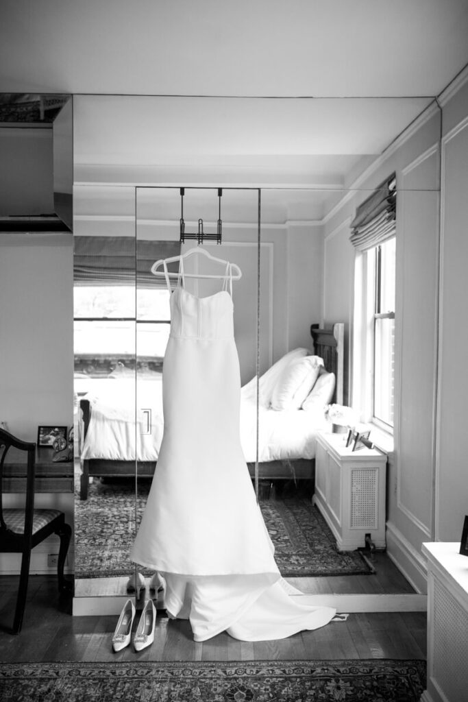 White wedding dress is on a hanger, hanging from a hook on a mirrored wall. The bride's heels are sitting below it. Black and white photograph.

Luxury NYC Wedding Photography. Manhattan Luxury Wedding Photographer. NYC Luxury Wedding. University Club Wedding Photographer.