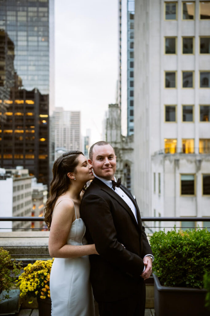 Bride stands behind groom with her head on his shoulder. Groom is smiling at the camera. They are standing on a rooftop in Manhattan with NYC in the background.

Luxury NYC Wedding Photography. Manhattan Luxury Wedding Photographer. NYC Luxury Wedding. University Club Wedding Photographer.