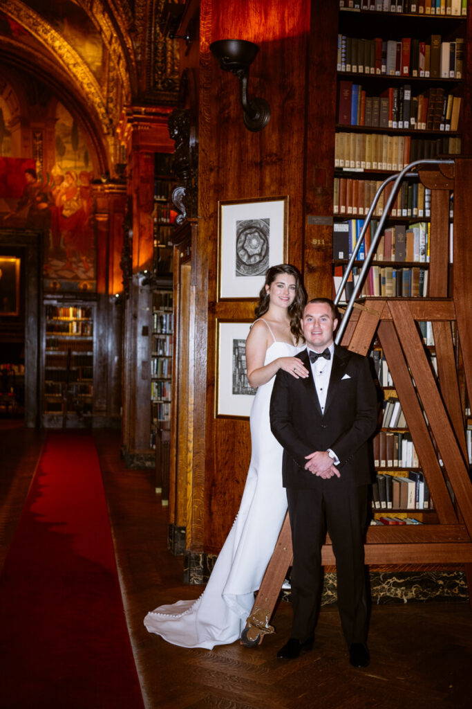 Bride and groom photographed in the library of the University Club. Bride is on a ladder slightly above the groom, with her hand on his shoulder. They are smiling at the camera.

Luxury NYC Wedding Photography. Manhattan Luxury Wedding Photographer. NYC Luxury Wedding. University Club Wedding Photographer.