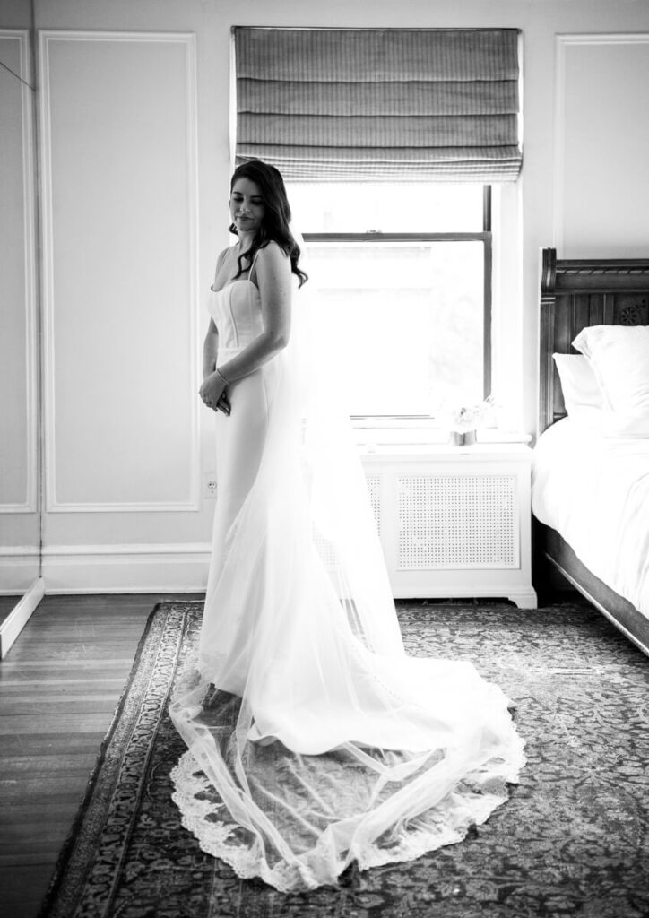 Bride is standing in a bedroom wearing her wedding dress and veil with lace details. She is smiling, looking at the ground toward the camera. Black and white photograph.

Luxury NYC Wedding Photography. Manhattan Luxury Wedding Photographer. NYC Luxury Wedding. University Club Wedding Photographer. Bride Portraits.