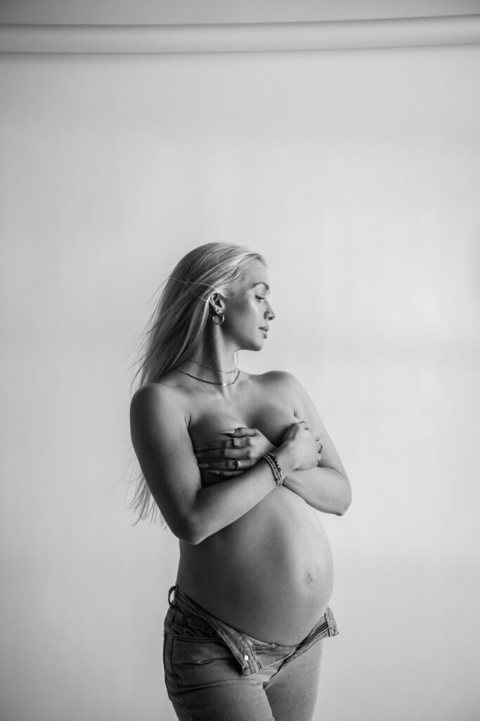 chic pregnant woman with belly showing looking off to the side peacefully with white backdrop photographed by Austin maternity photographer Kat Harris 