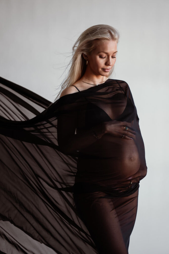 black chiffon fabric covering pregnant woman with her hands on her belly looking down in studio photographed by Austin maternity photographer Kat Harris 