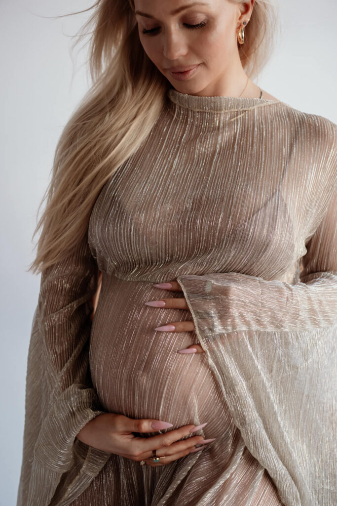 Flowy sheer gold maternity dress worn by pregnant woman with hair over right shoulder in natural light studio photographed by Austin maternity photographer KAT HARRIS