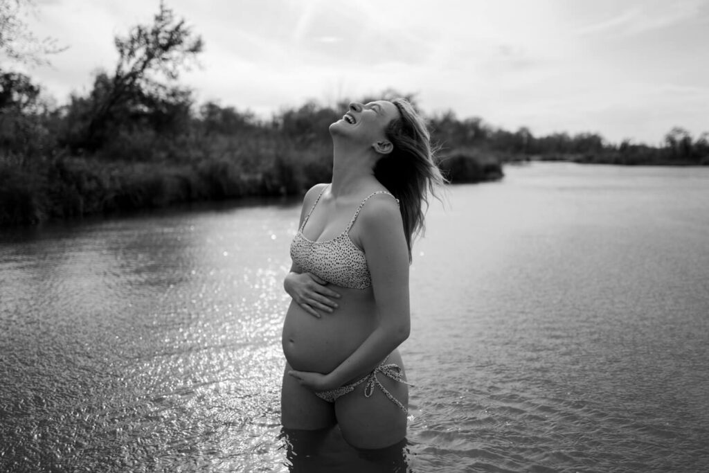 pregnant woman laughing with face towards the sky, thigh deep in river water outside Austin photographed by Austin maternity photographer Kat Harris.