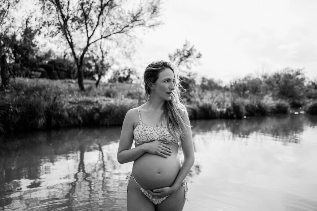 Portrait of pregnant mother hugging herself in the water in her bathing suit at sunset photographed by Austin maternity photographer Kat Harris.