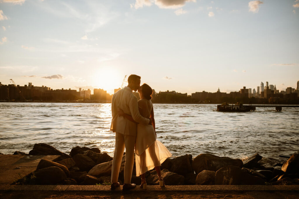 Golden hour engagement photo of engaged man and woman kissing each other lovingly waterfront in Williamsburg Brooklyn.