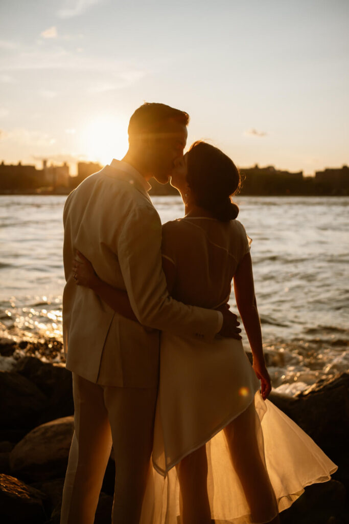 Couple kissing with arms wrapped around each other at sunset on the water in Williamsburg Brooklyn