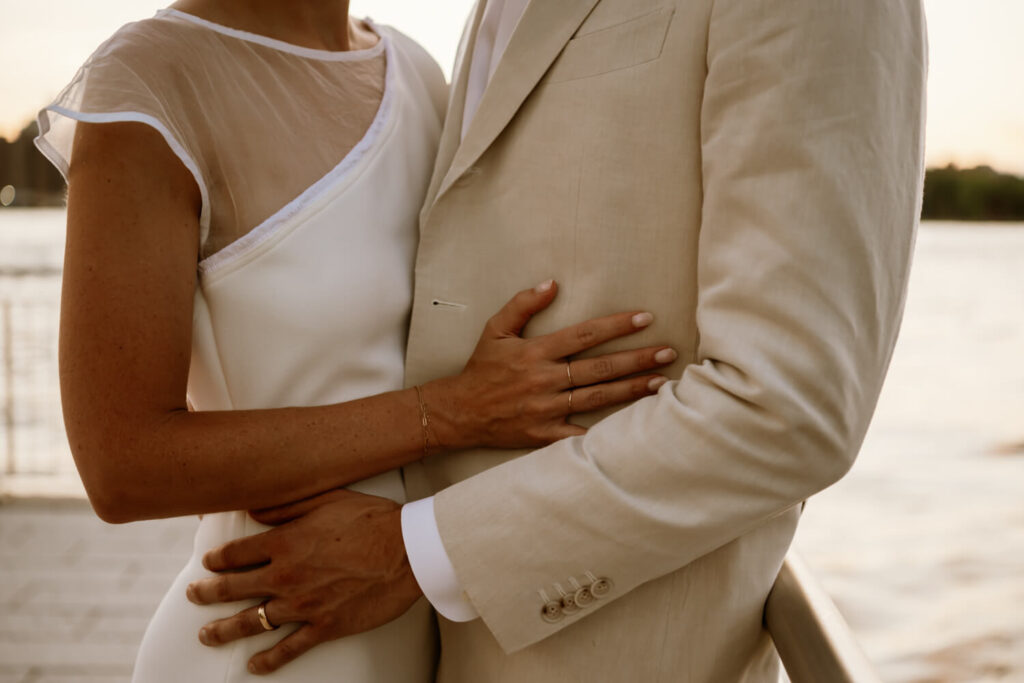 Bride and groom embrace at Domino Park's waters edge on a summer's night at sunset.