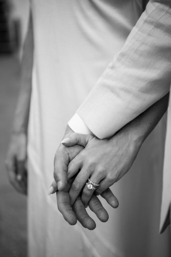 Black and white engagement photo close-up shot of the brides engagement rings as she holds her fiancé's hand.