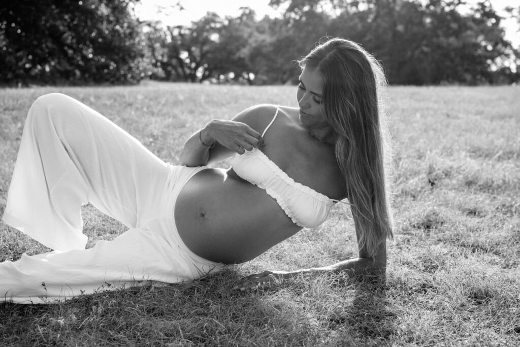 black and white timeless portrait in natural light of pregnant woman lying on the ground looking towards her baby bump photographed by Austin maternity photographer Kat Harris.