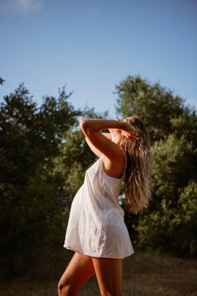 Profile photo of pregnant women in a white slip dress leaning her head back fixing her hair in the soft morning light photographed by Austin maternity photographer Kat Harris.