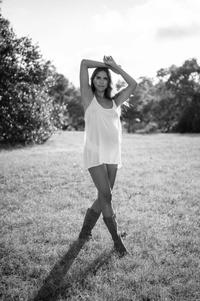 chic black and white portrait of pregnant mother wearing a white slip dress and riding boots in a field photographed by Austin maternity photographer Kat Harris.