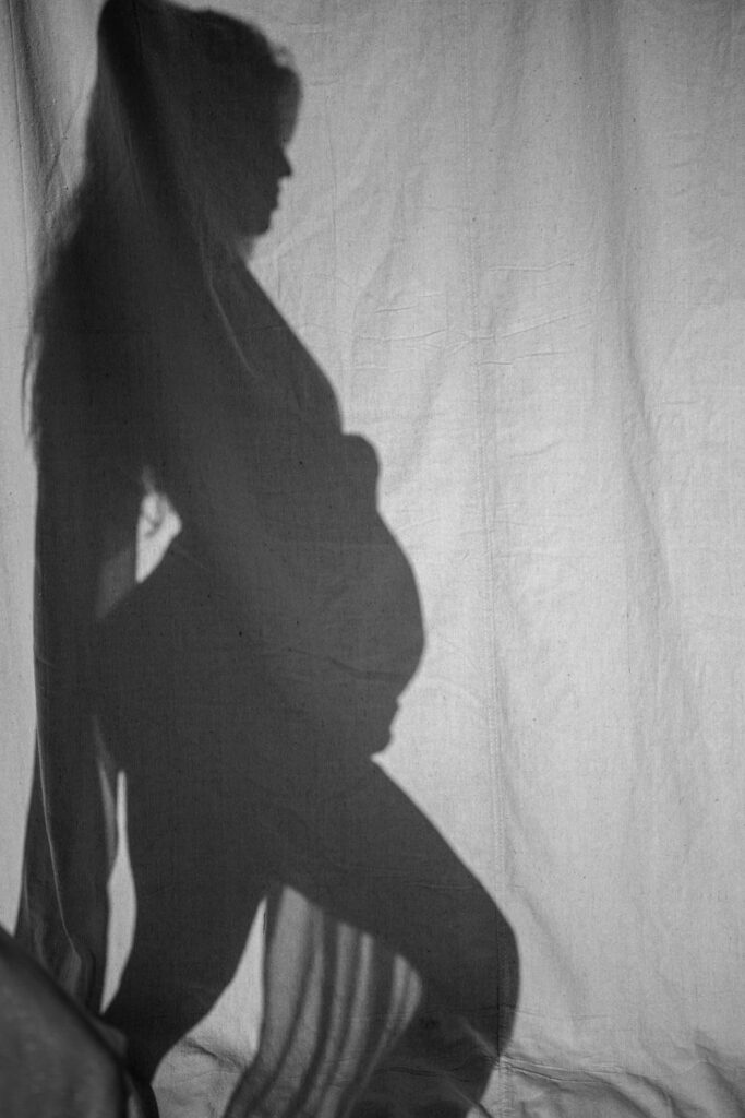 black and white artsy photo of the shadow of a pregnant mom holding her baby bump draped in sheer fabric photographed by Austin maternity photographer Kat Harris.