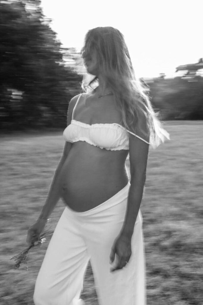 blurred black and white portrait of pregnant woman in a field with white bralette and pants photographed by Austin maternity photographer Kat Harris.