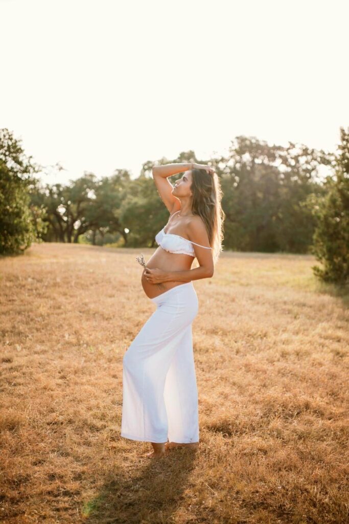 profile photo of pregnant woman with one hand on her baby bump and the other in her hair standing in a golden field photographed by Austin maternity photographer Kat Harris.