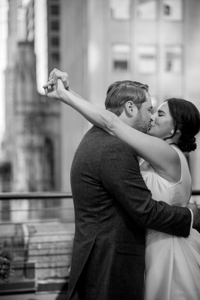 Bride and groom share an embrace and kiss during bridal portraits overlooking the busy streets of Manhattan on the University Club of NY's rooftop terrace photographed by New York City wedding photographer Kat Harris.