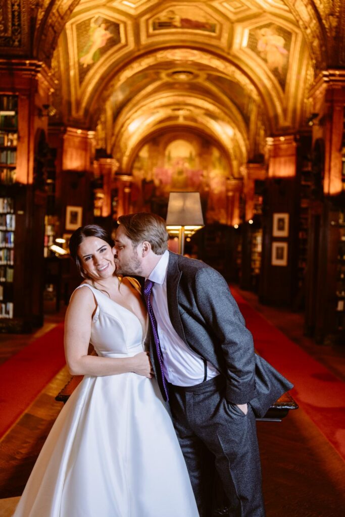 groom kissing bride on the cheek in the University Club of NY iconic library with red carpet photographed by New York City wedding photographer Kat Harris.