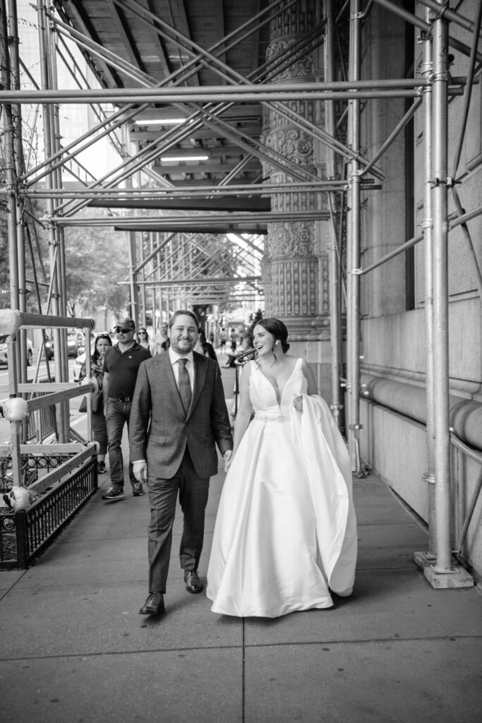 bride and groom walk down the busy streets of New York City laughing during their editorial portraits outside of University Club of New York City photographed by New York City wedding photographer Kat Harris.