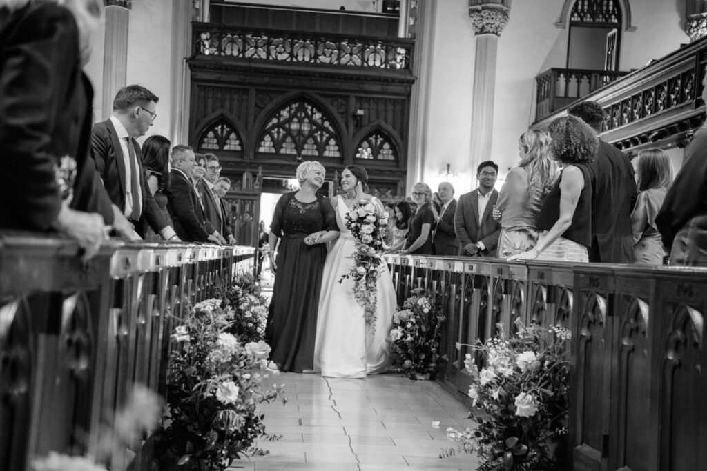 mother of the bride and bride share a quite moment as they walk down the aisle towards the groom at The First Presbyterian Church on 12th street and 5th ave photographed by New York City wedding photographer Kat Harris.