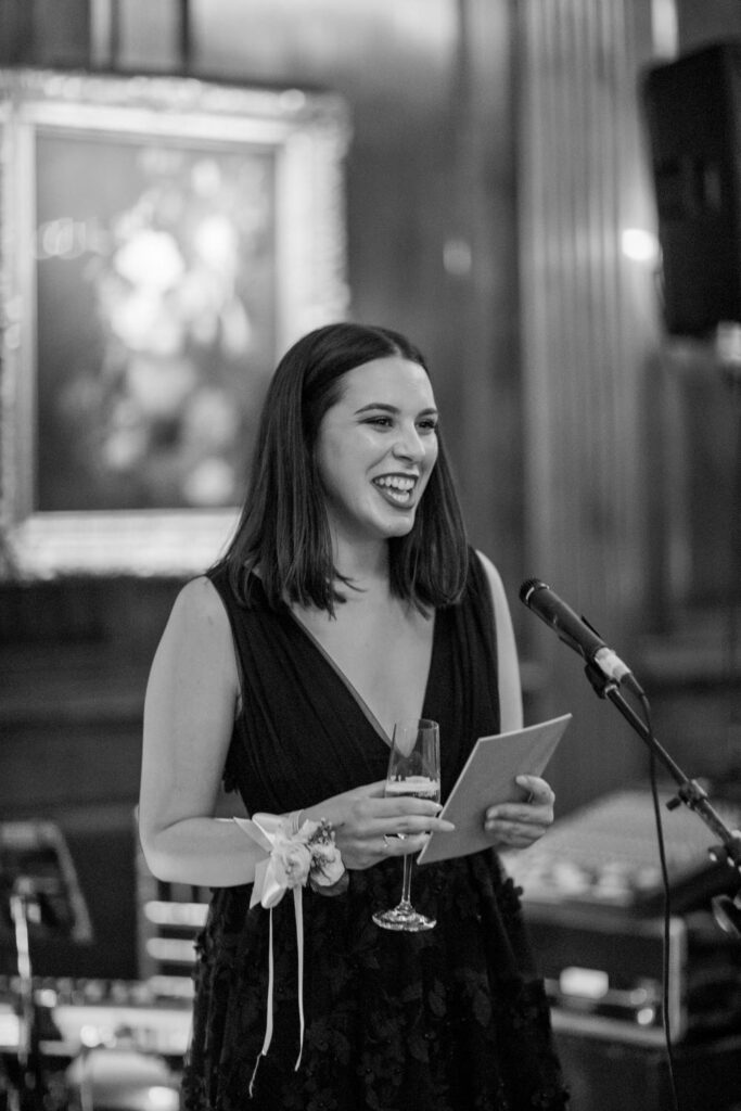 maid of honor smiles towards the newly married couple as she delivers a toast during the University Club of New York City wedding reception photographed by New York City wedding photographer Kat Harris.