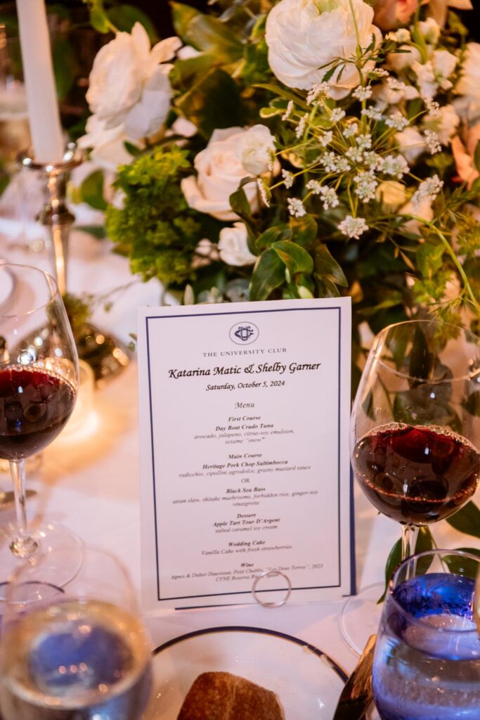 photo of the menu card on the table surrounded by food, red wine, and flowers photographed by New York City wedding photographer Kat Harris.