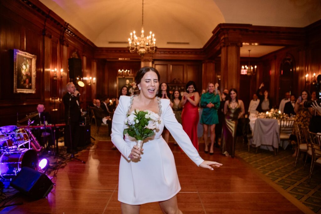 Bride changed into short reception wedding dress and dances as she prepares for the bouquet toss at her Manhattan University Club wedding reception photographed by New York City wedding photographer Kat Harris.