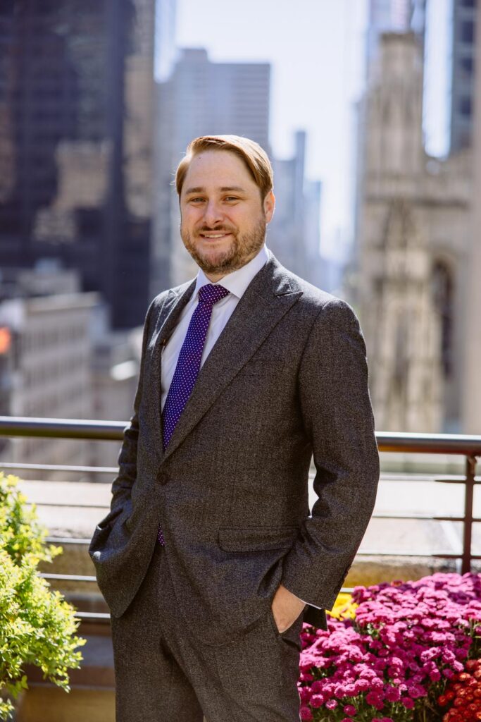 Portrait of Groom in grey suit with purple tie on the rooftop terrace of the University Club of New York City overlooking the busy NYC streets photographed by New York City wedding photographer Kat Harris.