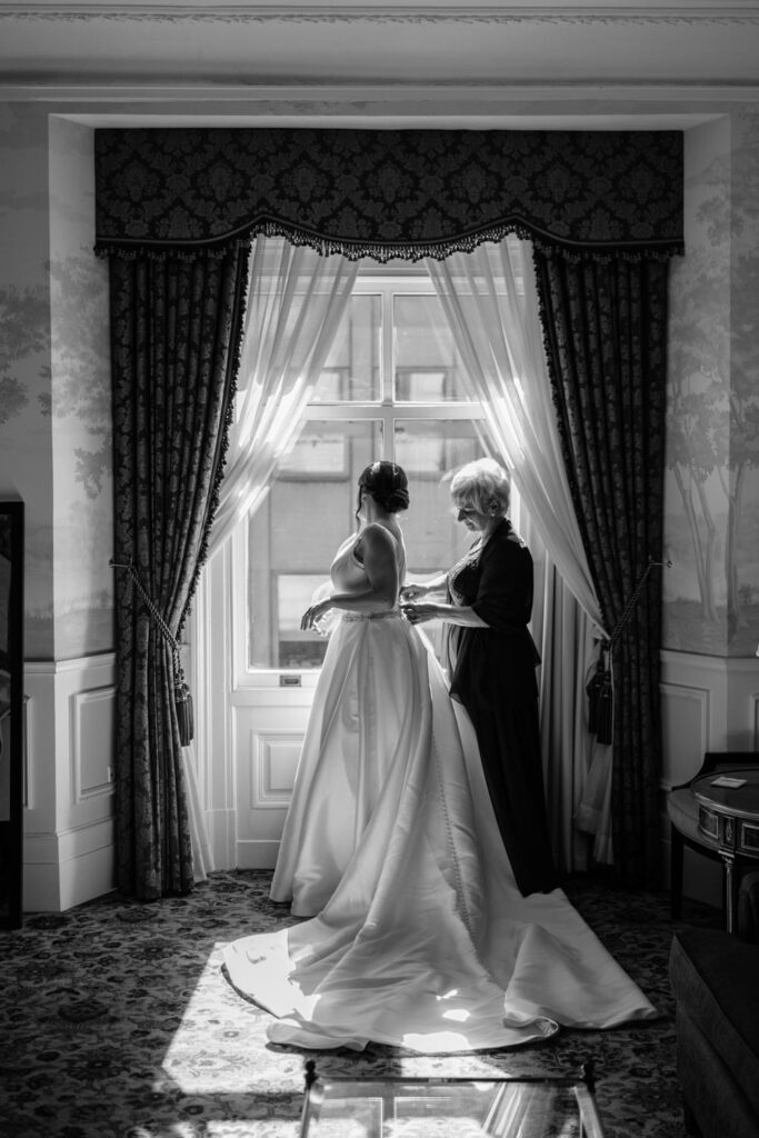 Black and white photo of the Mother of the bride helping bride put on her custom Pronovias wedding gown photographed by New York City wedding photographer Kat Harris.